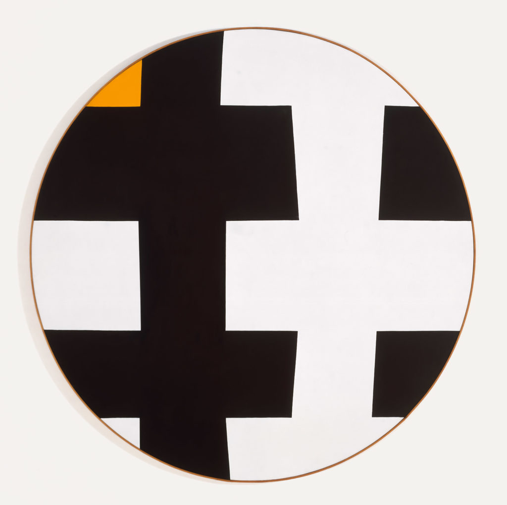 Circular Tondo, black and white shape pattern fitting together cropped tight by the circle one of the white edges is replaced with a deep yellow which verges on orange. The work has a very thin wood frame which adds a bit of warmth to the work.