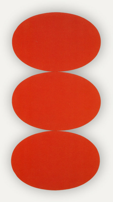 Three tomato red oval canvases wider than tall perfectly balanced on each other.